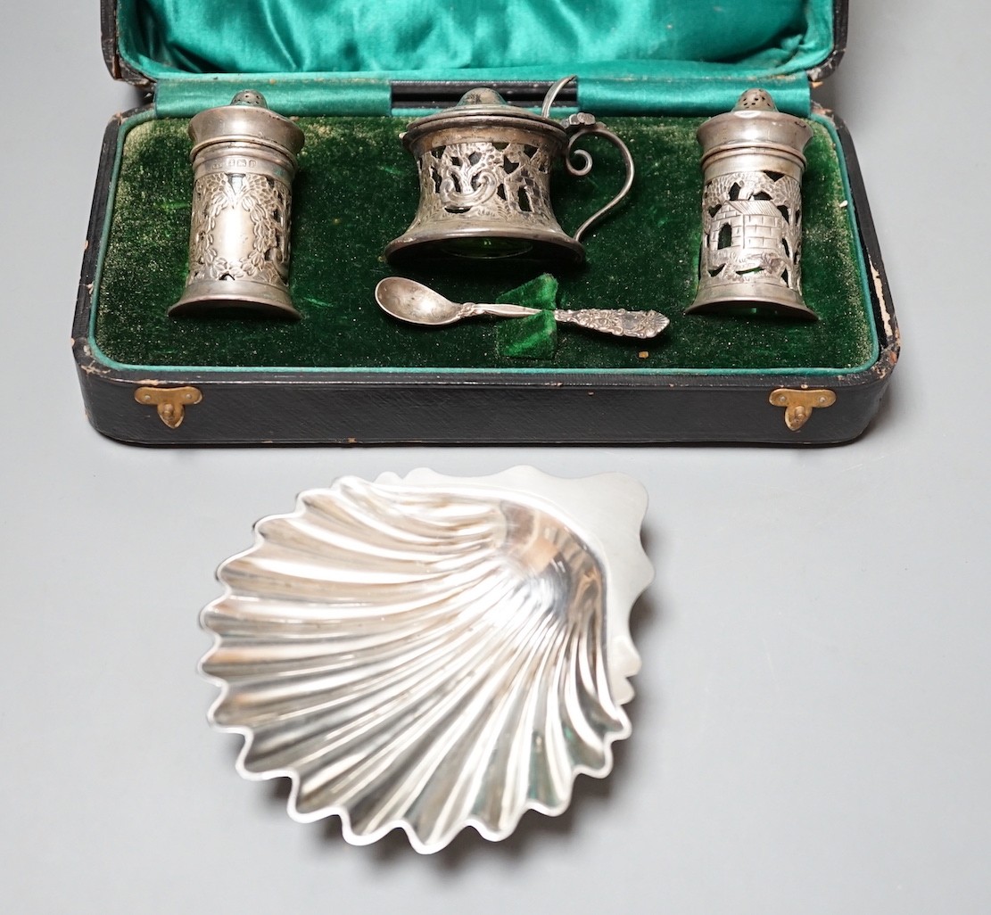 A late Victorian silver butter shell, London, 1892, 11.5cm and a cased George V silver three piece condiment set with green glass liners.